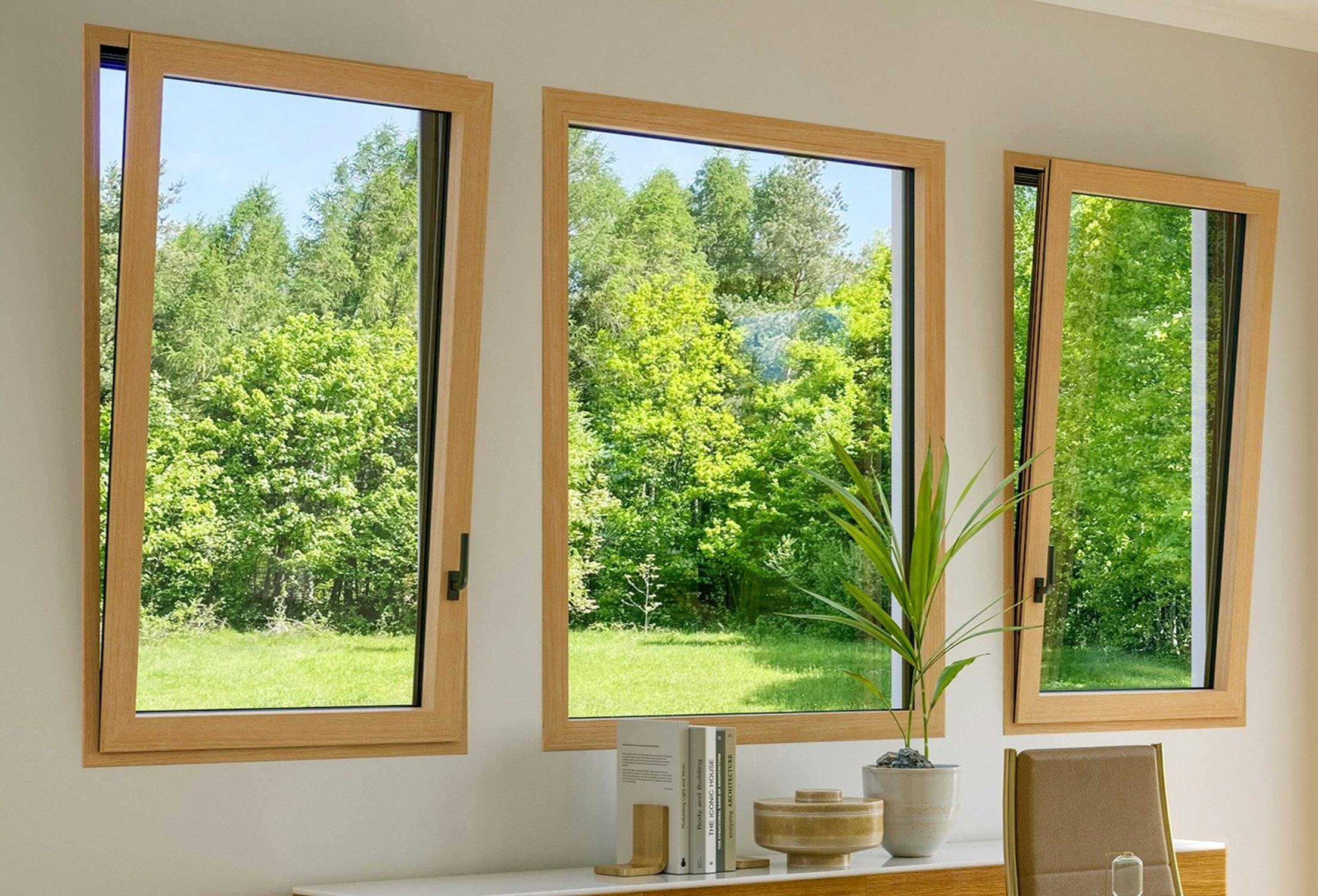 Modern living room with three wood framed tilt turn windows, two open and one closed, overlook a green lawn and trees.