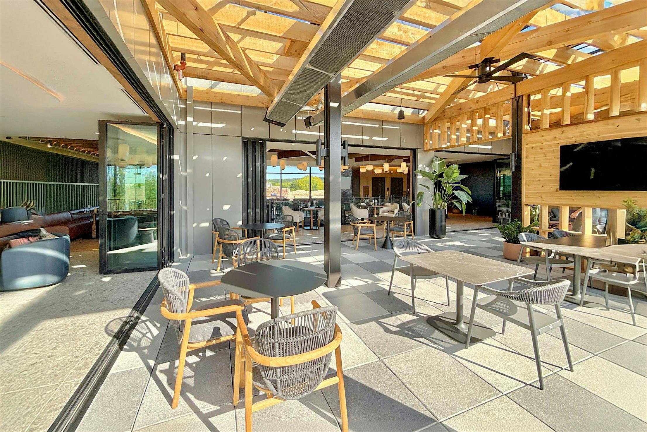 Spacious indoor seating area with bifold glass doors enhance the airy ambiance, while tables and chairs are neatly arranged on a tiled floor.