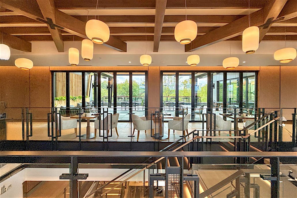 Modern restaurant interior with wooden beams and hanging round lights, featuring tables and chairs set by large bifold glass doors.