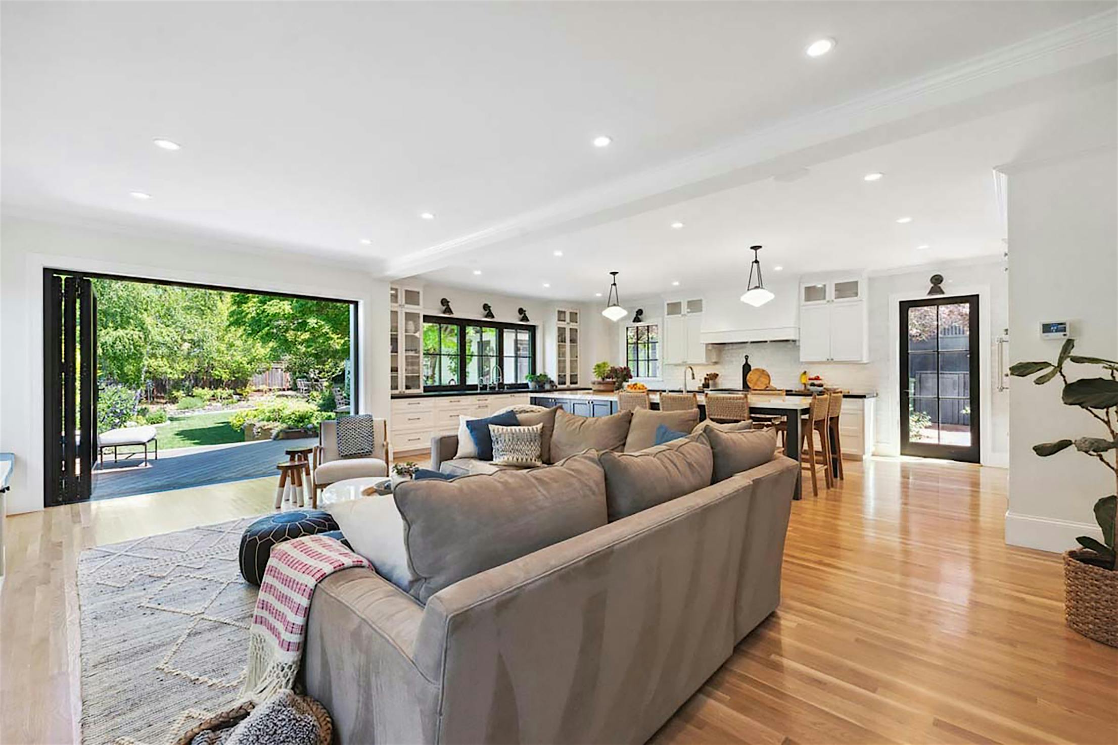 Spacious open-plan living area leading to large folding glass walls that open to a lush garden, offering seamless indoor-outdoor living.