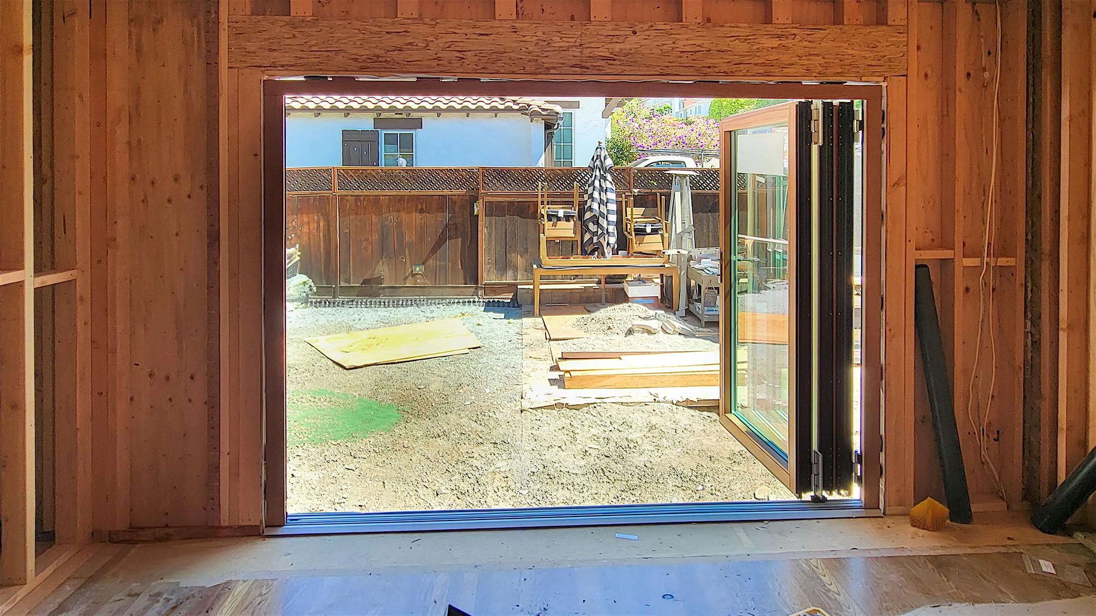 Partially constructed wooden frame of a room with large open folding glass doors leading to a backyard,