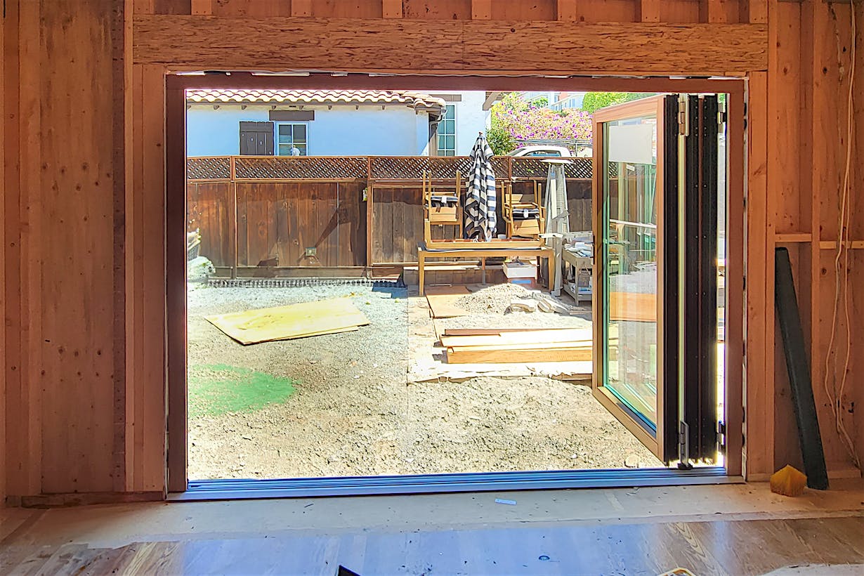 Partially constructed wooden frame of a room with large open folding glass doors leading to a backyard,