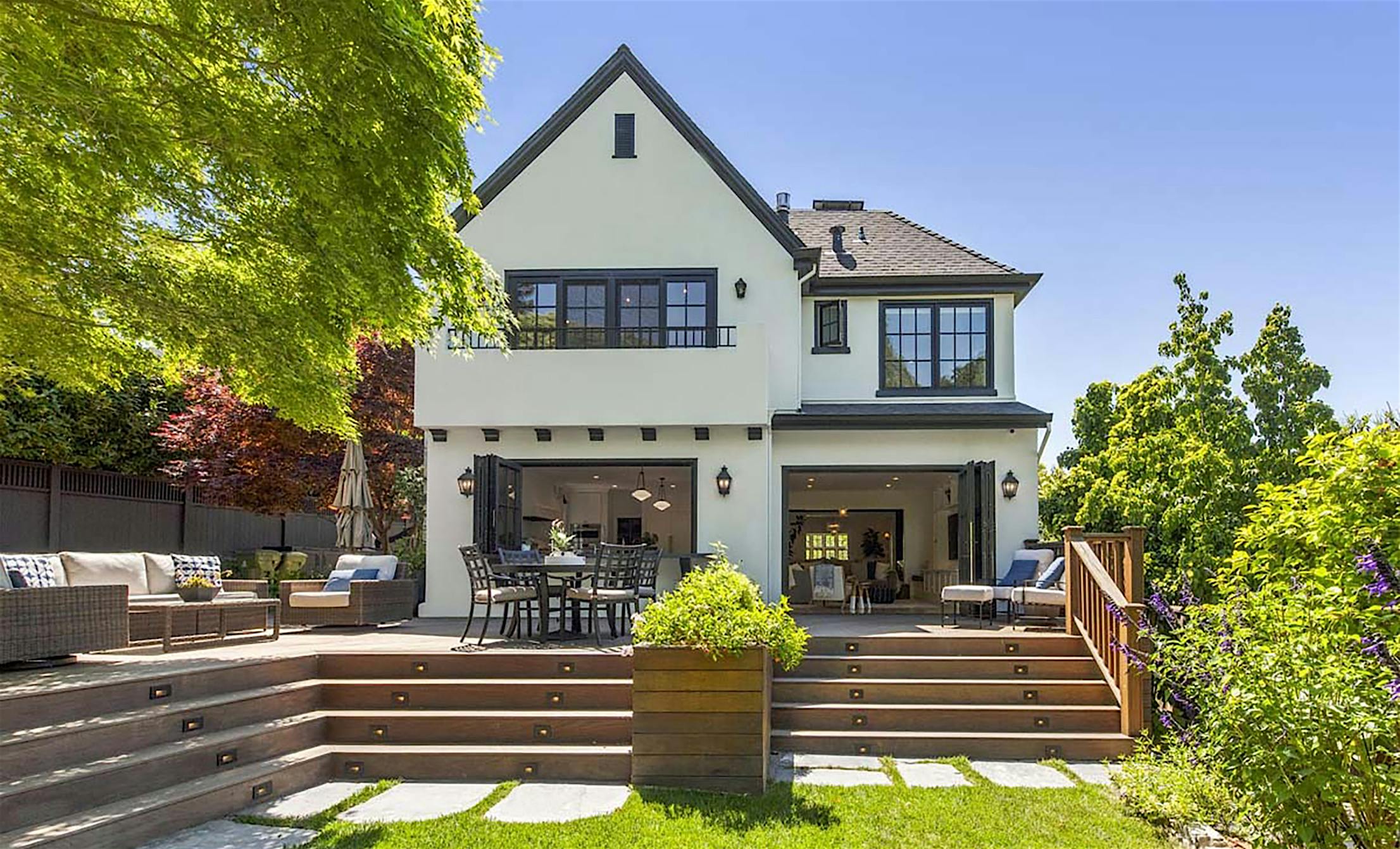 A beautifully remodeled two-story American Craftsman house featuring a gabled roof, large folding glass doors, and an outdoor deck with seating.