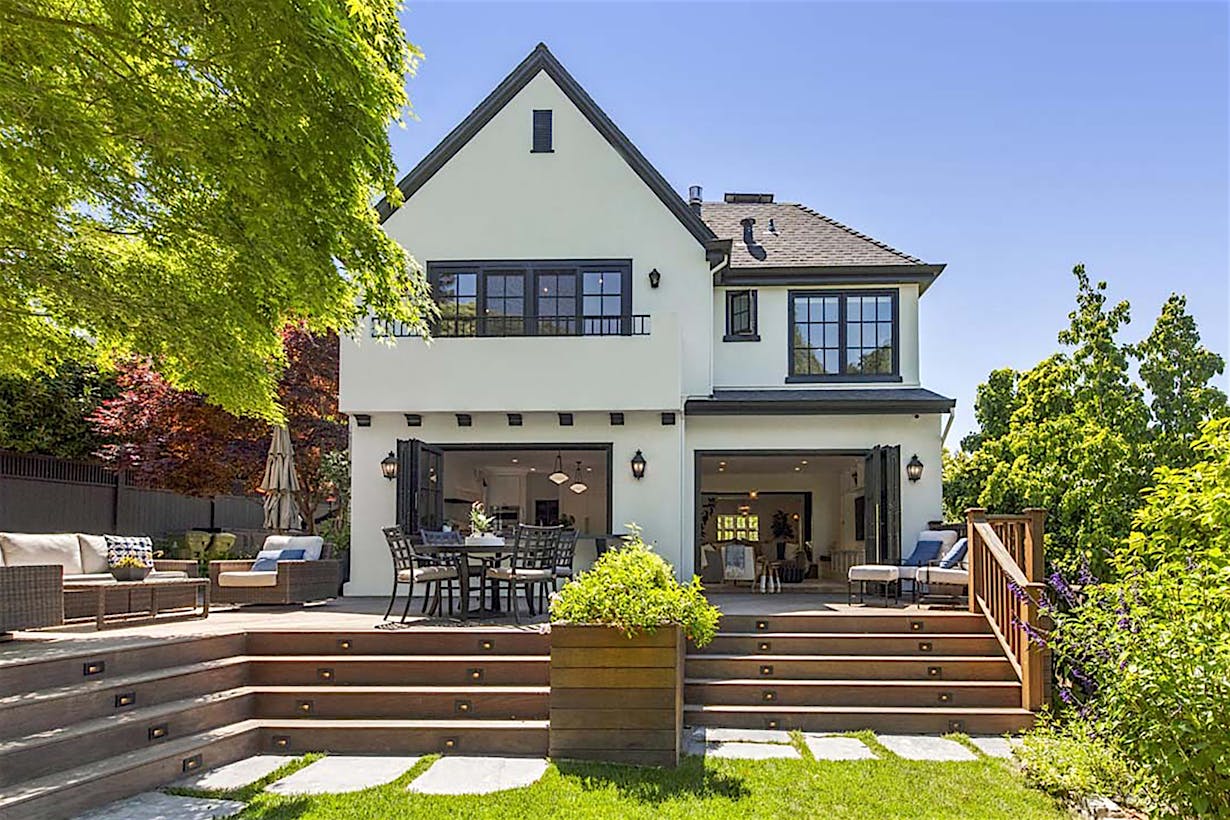 A beautifully remodeled two-story American Craftsman house featuring a gabled roof, large folding glass doors, and an outdoor deck with seating.