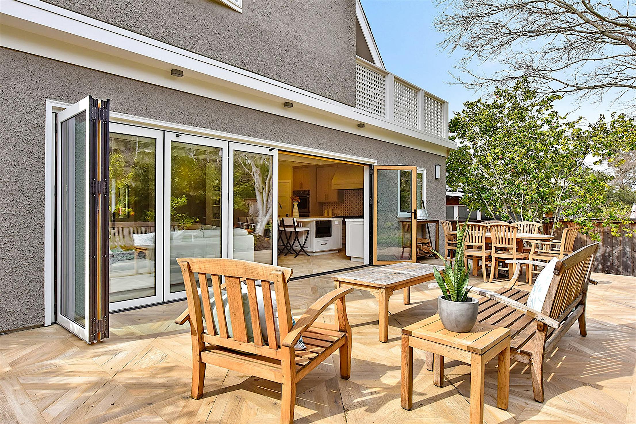 A wooden patio set with chairs and a table graces the wooden deck, next to folding glass patio doors leading into the house.