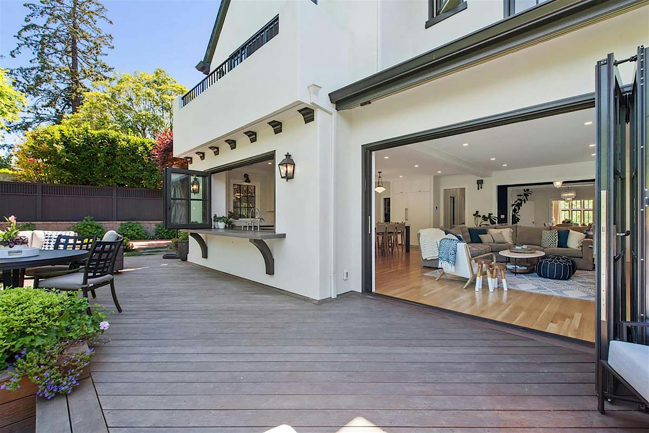 Spacious patio with wooden decking, outdoor seating, and large folding glass walls leading to a modern living room with light-colored furniture, perfectly blending style and functionality for any remodeling project.