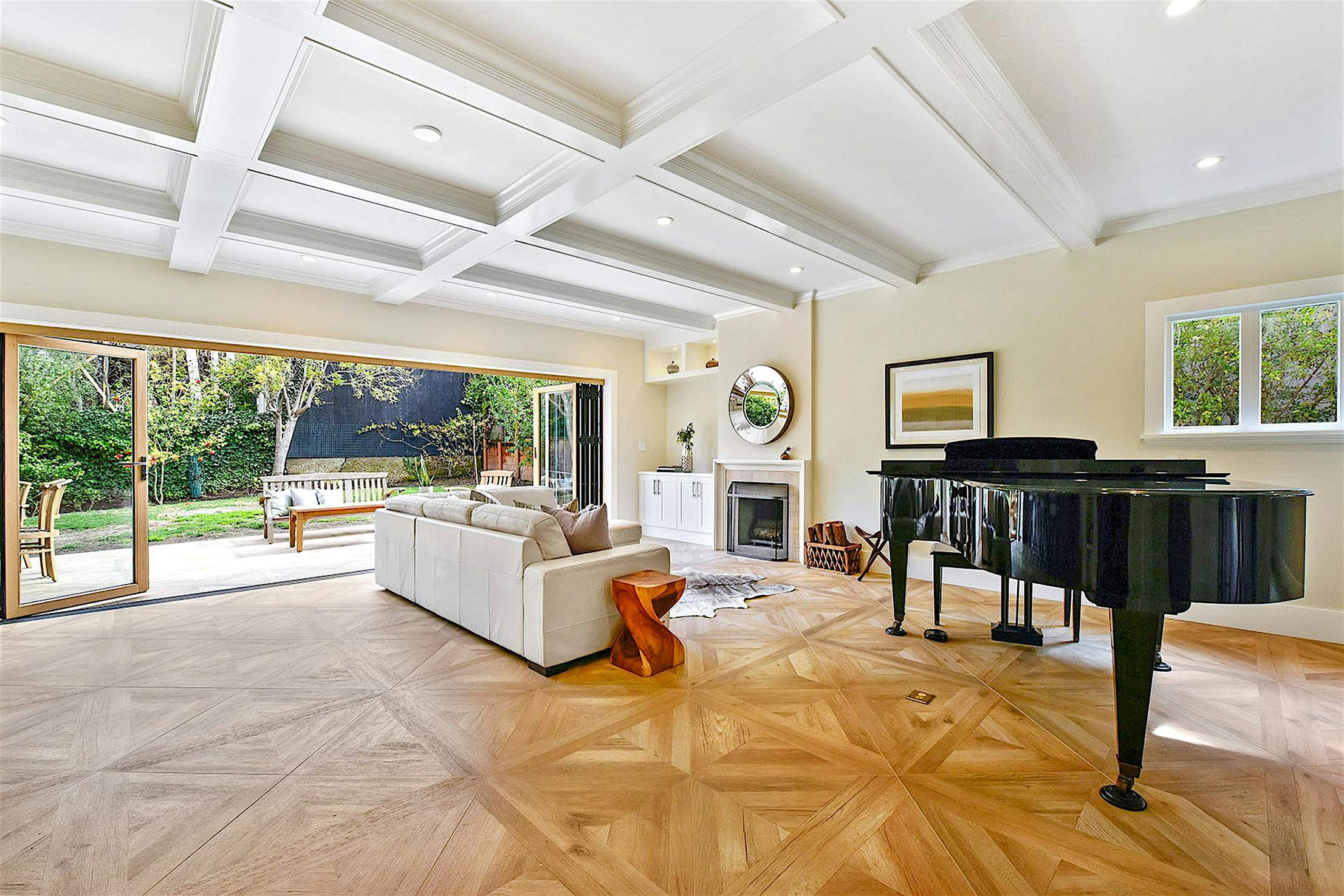 Spacious living room with large glass folding doors open to a patio and garden. Light wooden floor with a geometric pattern adds charm to the Craftsman house remodeling.