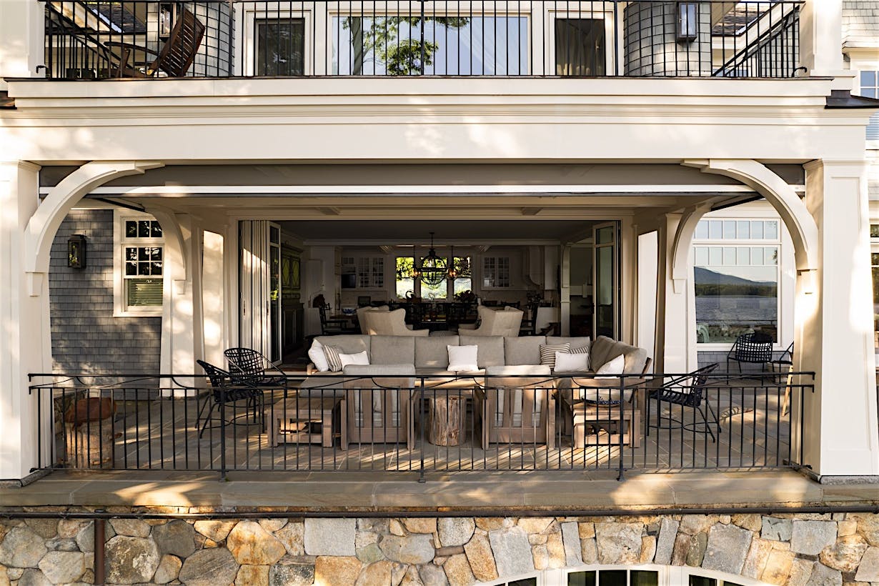 Spacious patio with a white frame and stone foundation, featuring outdoor furniture and white glass patio doors.