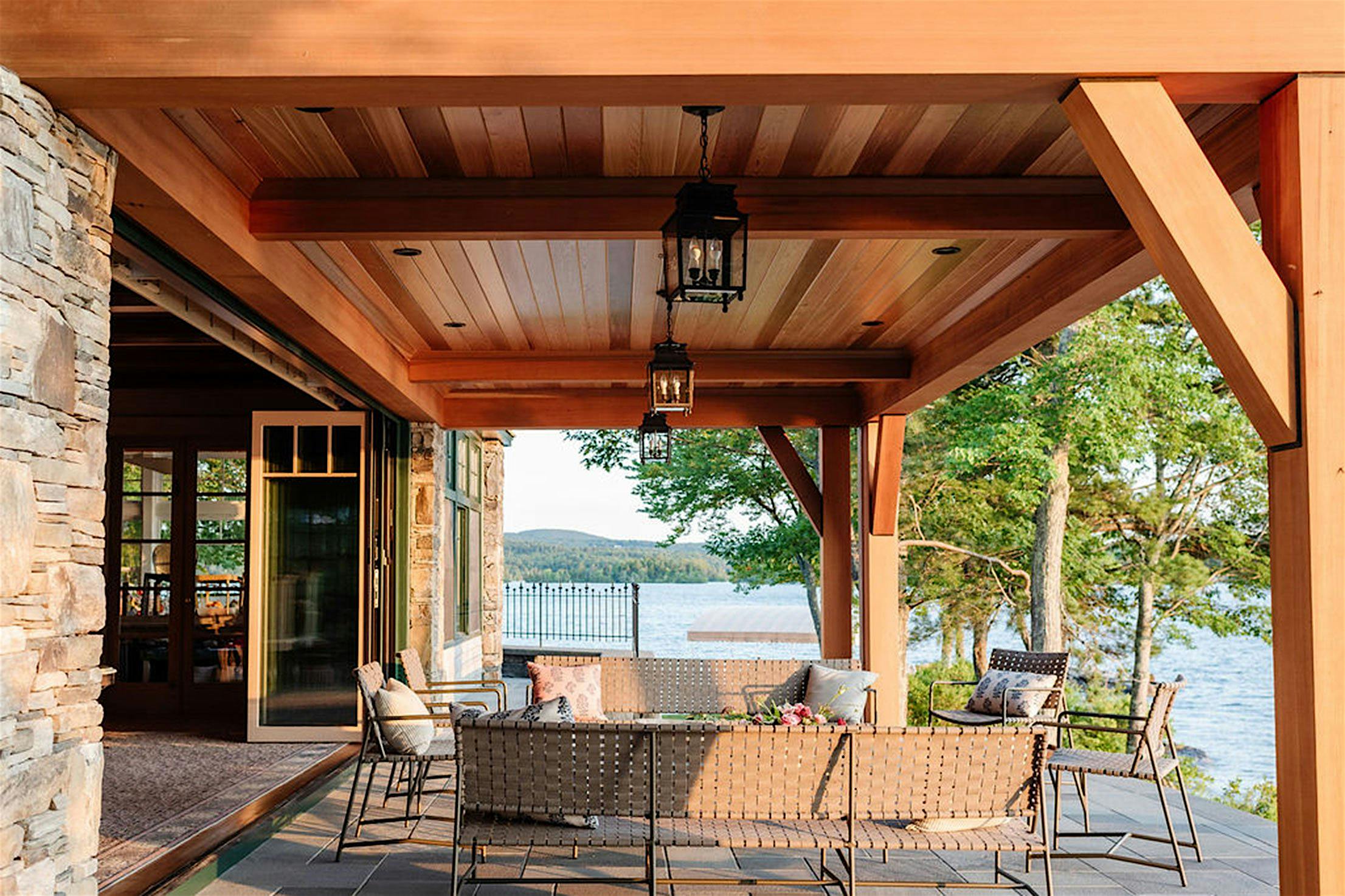 Covered patio with wicker furniture, glass patio doors overlooking a lake with trees and hills in the background.