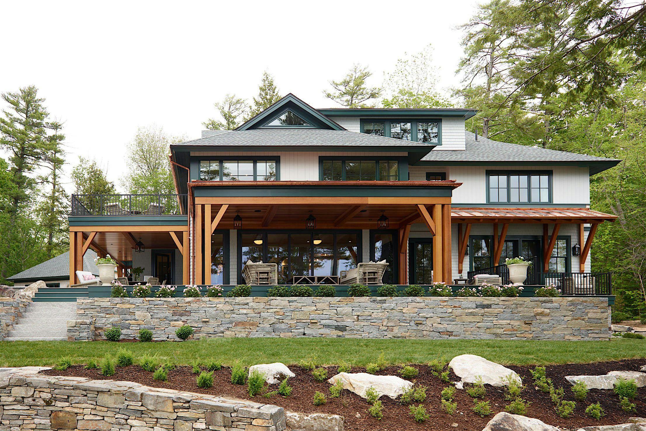 Two-story house with wooden beams, stone base, and a large covered patio featuring folding patio doors,