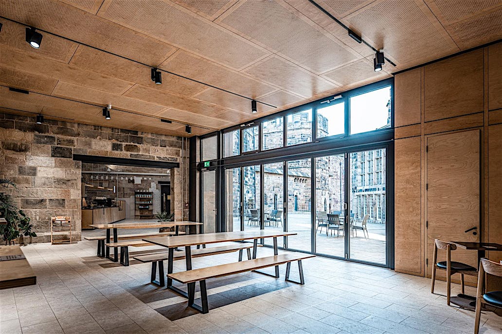 A rustic wooden dining area features long tables and benches, framed by large folding doors designed to meet performance challenges.