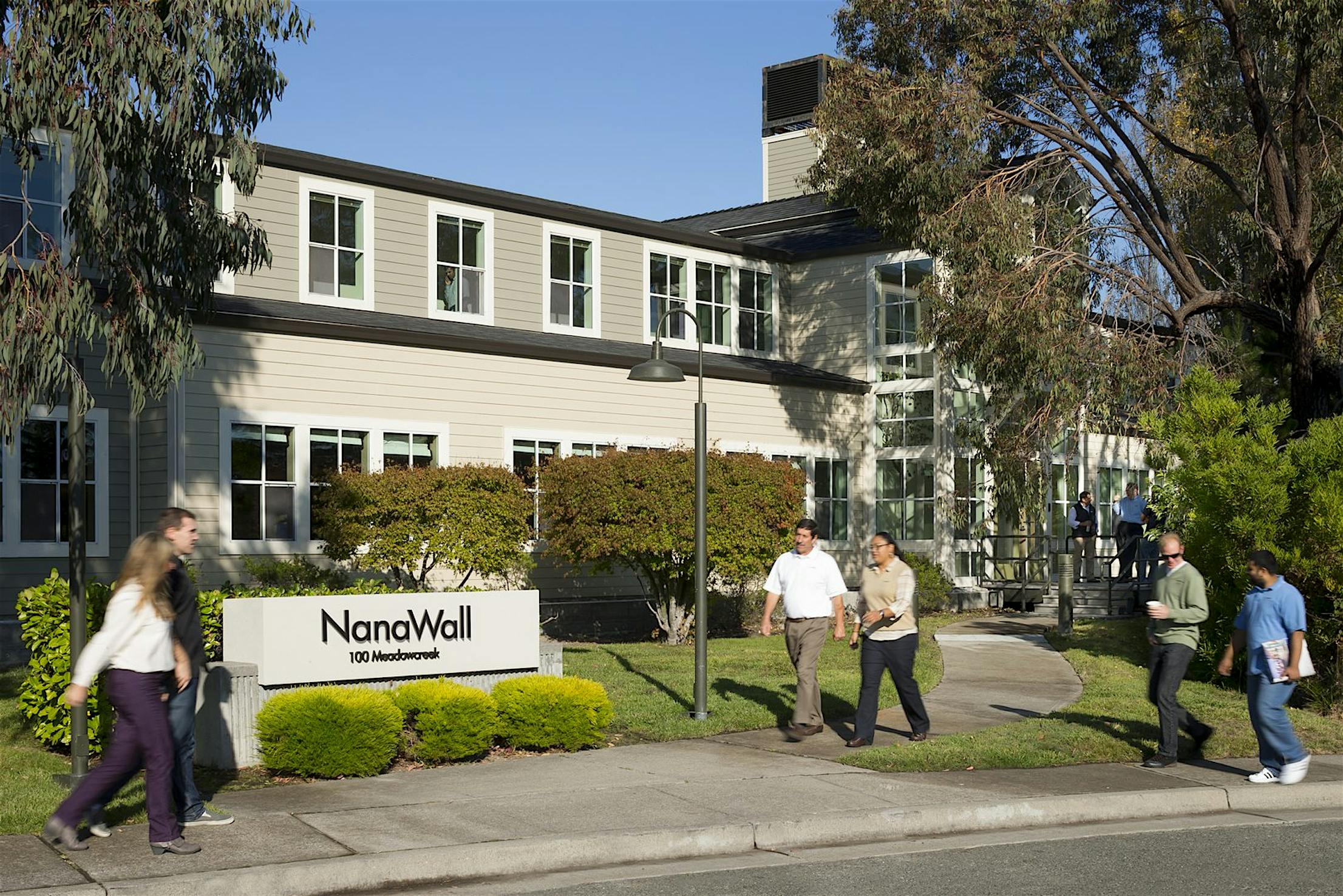 People walk along the sidewalk in front of the two-story NanaWall glass doors HQ building.