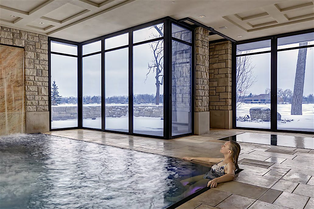 Modern indoor pool with stone waterfall and glass doors overlooking snowy landscape