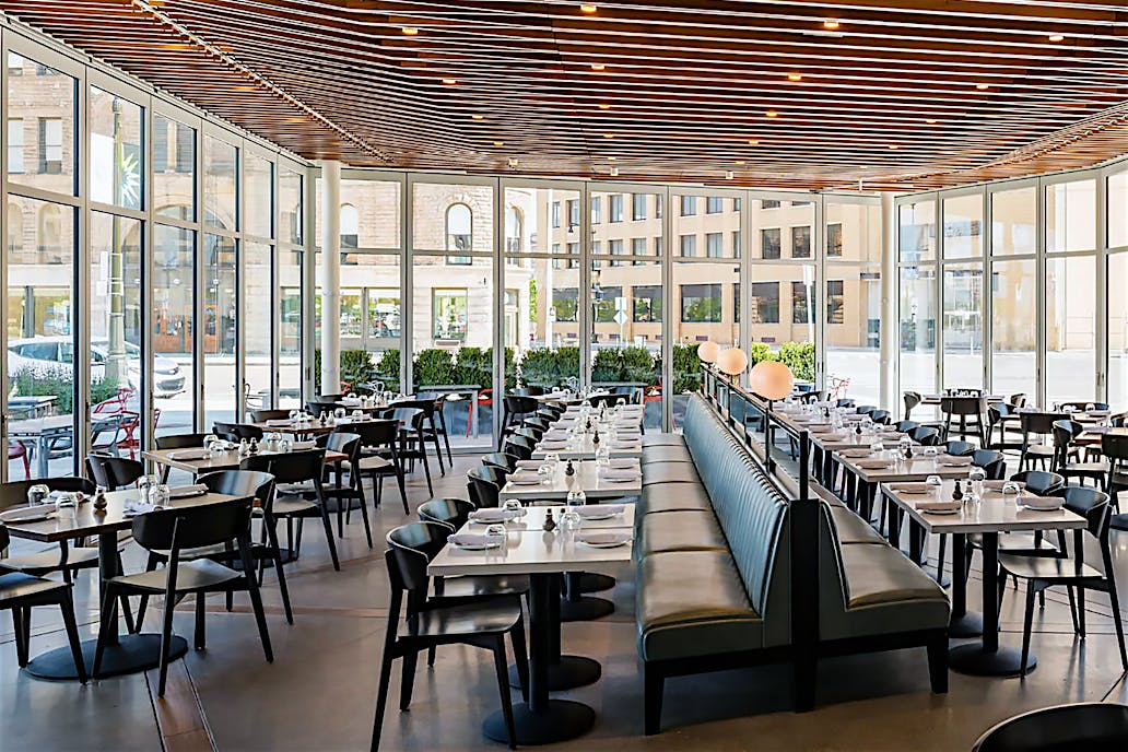 Stylish modern restaurant with floor-to-ceiling glass walls, sleek interior seating, and street-facing glass doors.