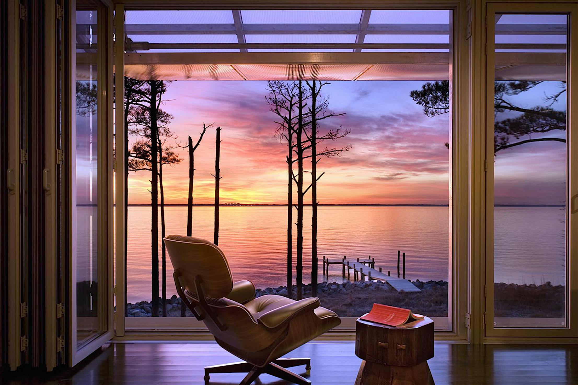 Modern living room with large glass doors opening to a lakeside view at sunset.