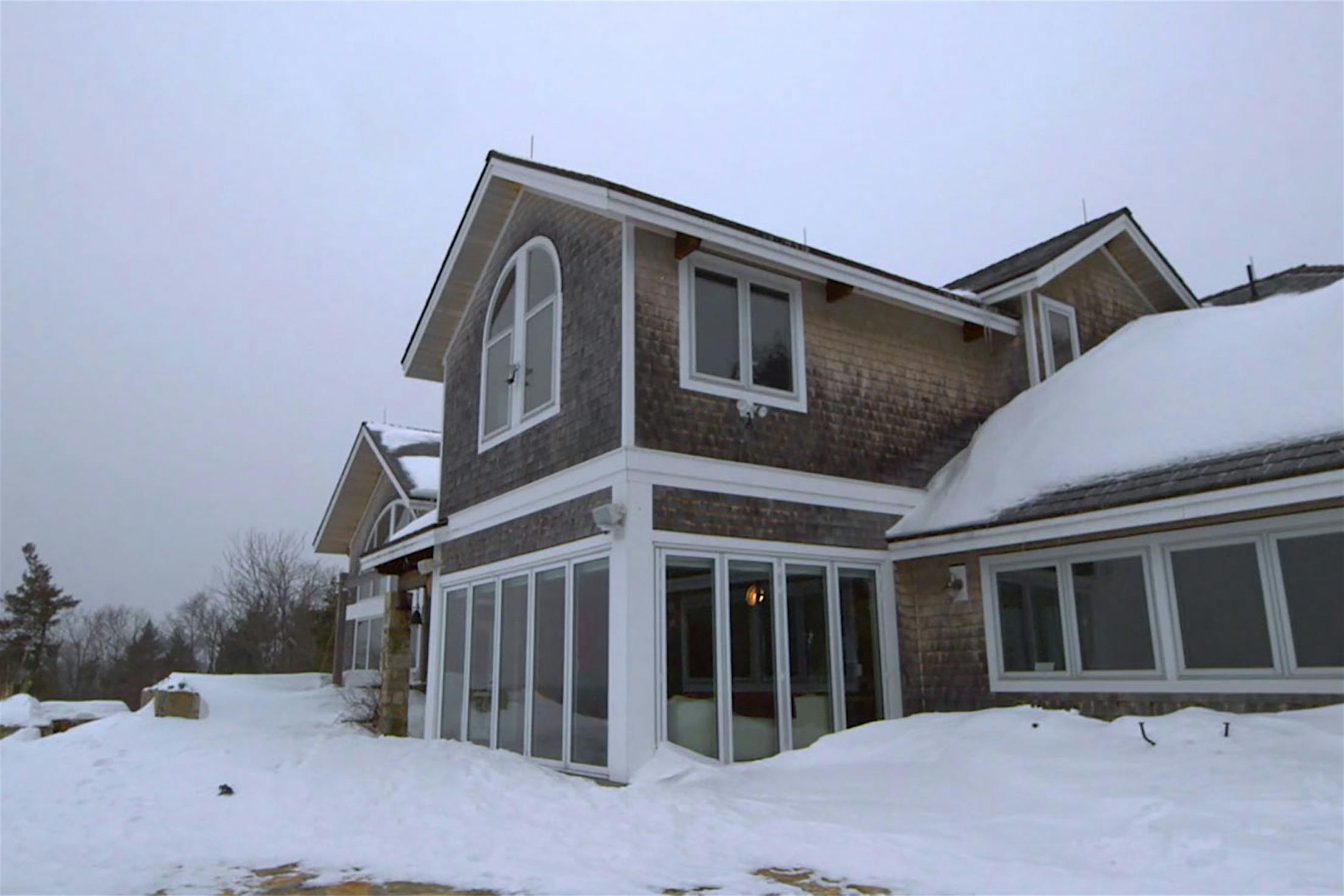 A large house with multiple windows and high weather performance bifold glass doors stands in a snowy, overcast landscape, its roof blanketed in cold weather snow.