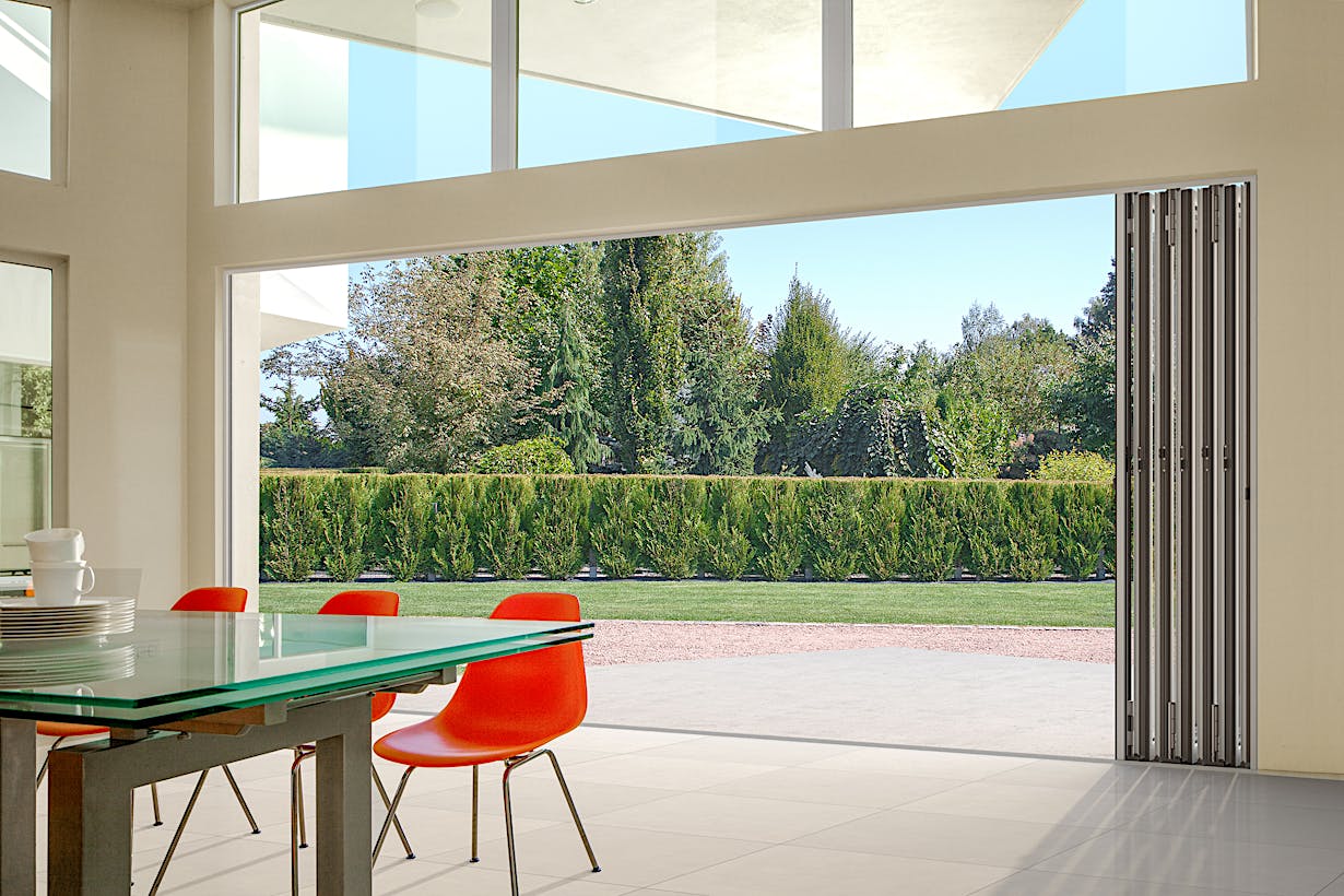 A sleek dining room with a slim aluminum framed glass walls - opened doors view