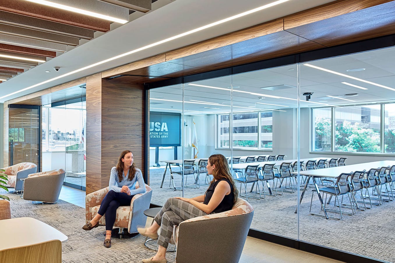 Two women sitting in chairs in a conference room with frameless glass walls