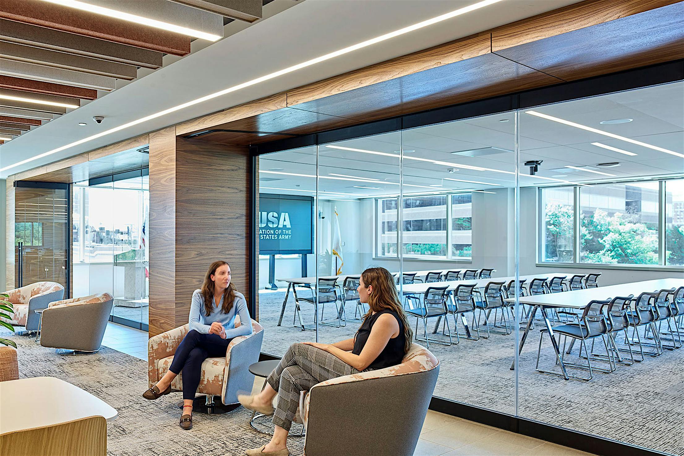 Two women sitting in chairs in a conference room with frameless glass walls