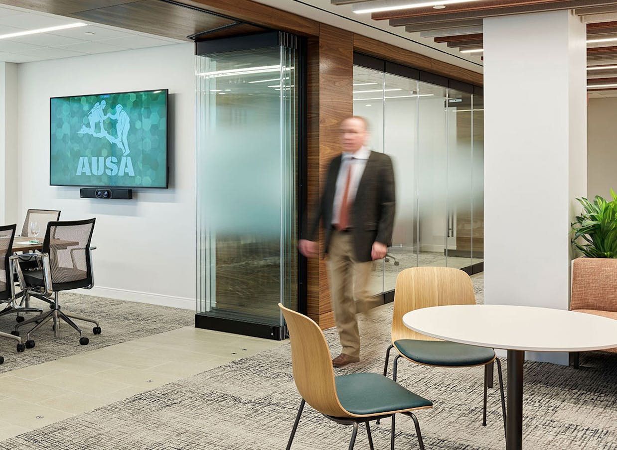 A man walks through an office conference room with frameless glass partitions