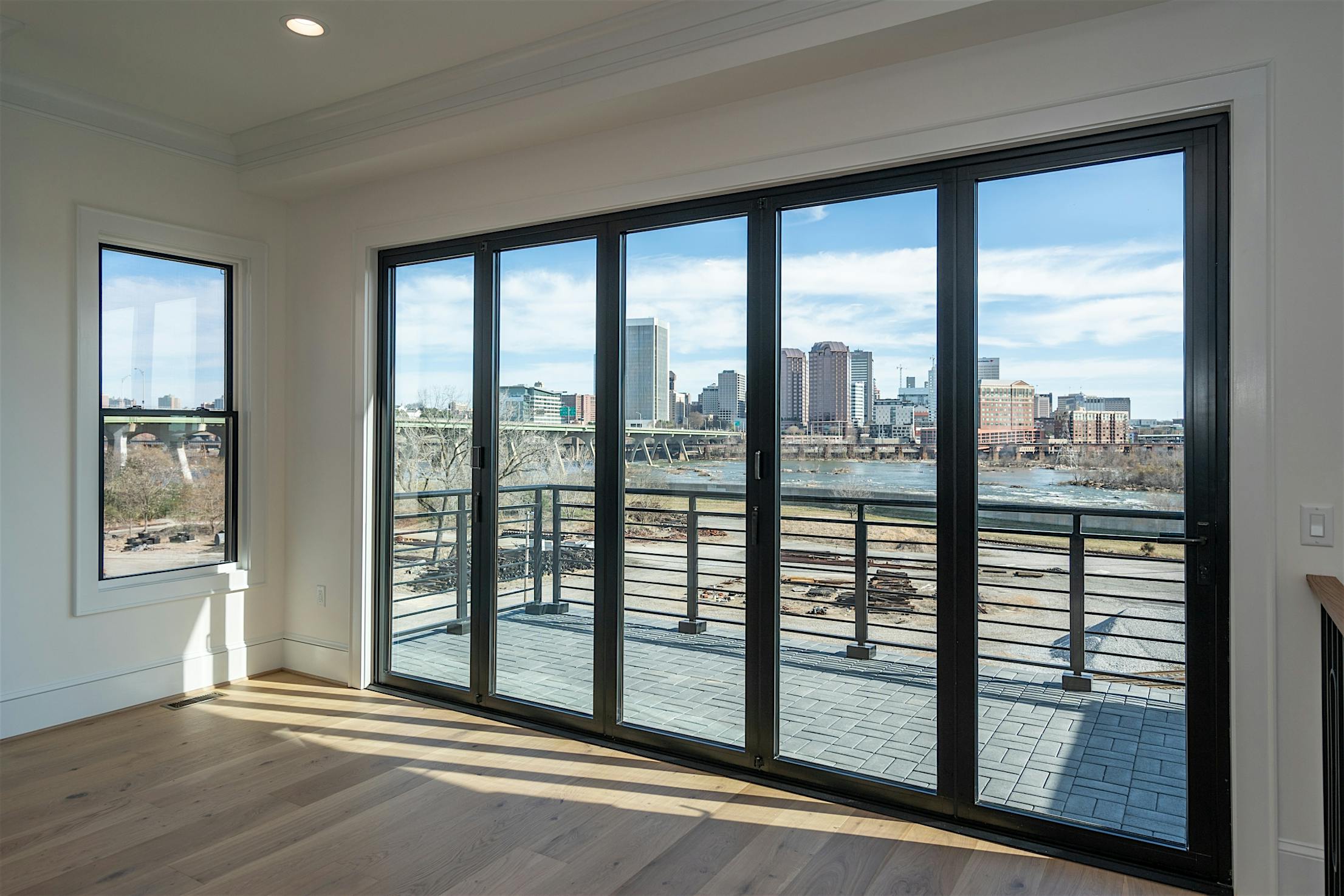 View of a city skyline and river through large glass doors in a modern room with hardwood floors and white walls.