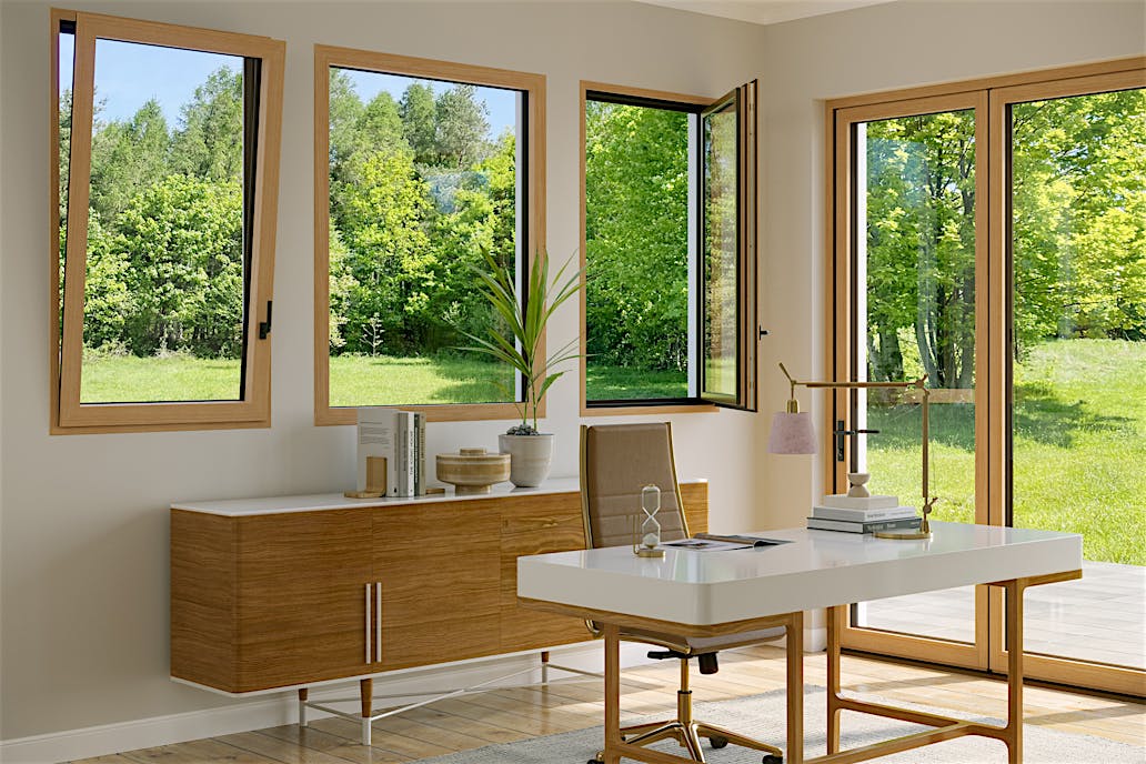 An office with a wooden table features Generation 4 folding glass walls and tilt turn windows, offering a uniform aesthetic and framing views of trees with yellow autumn leaves outside.