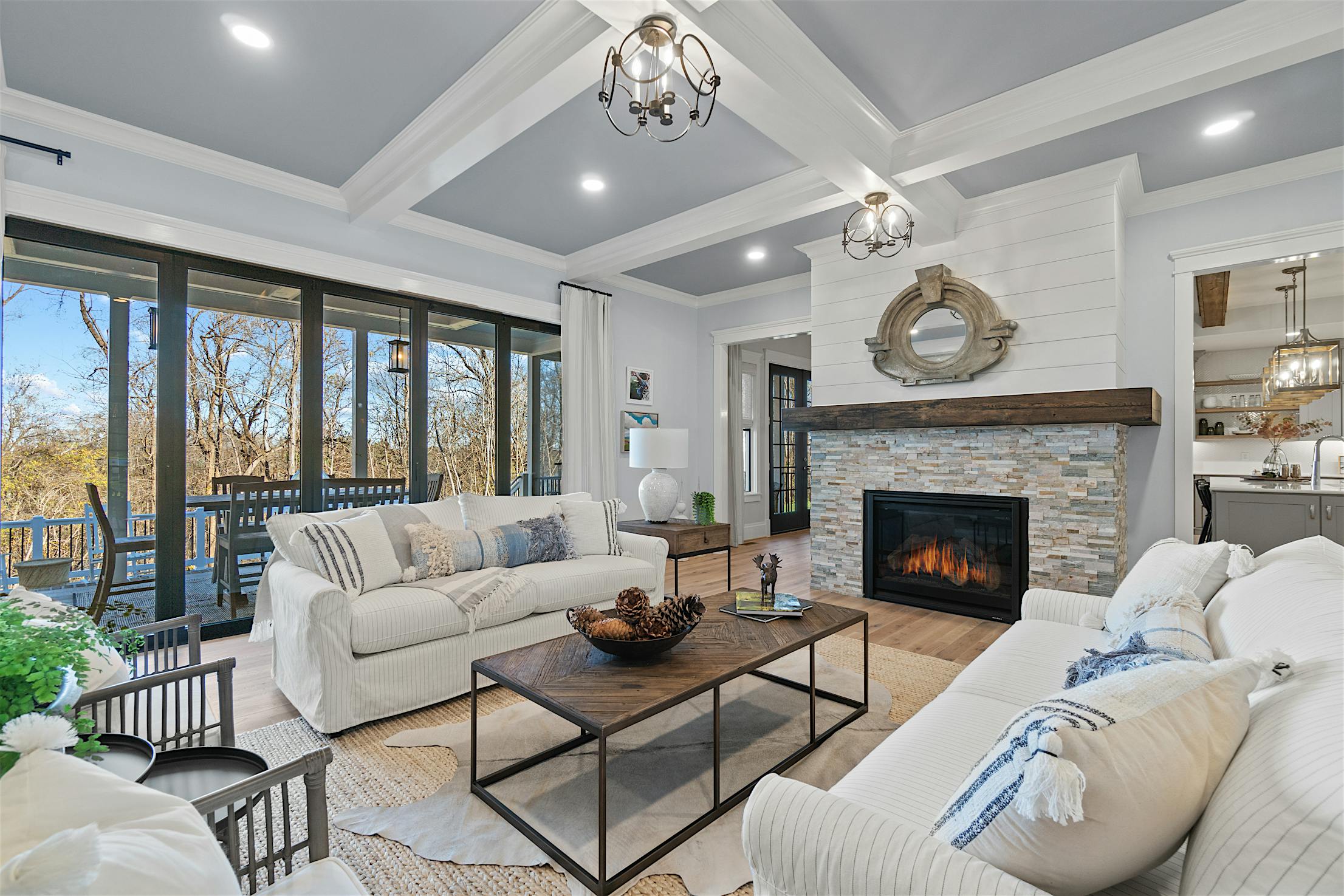 Modern Living room features white walls, a beamed ceiling, modern light fixtures, and folding glass doors that seamlessly connect indoor comfort with the natural beauty outside.