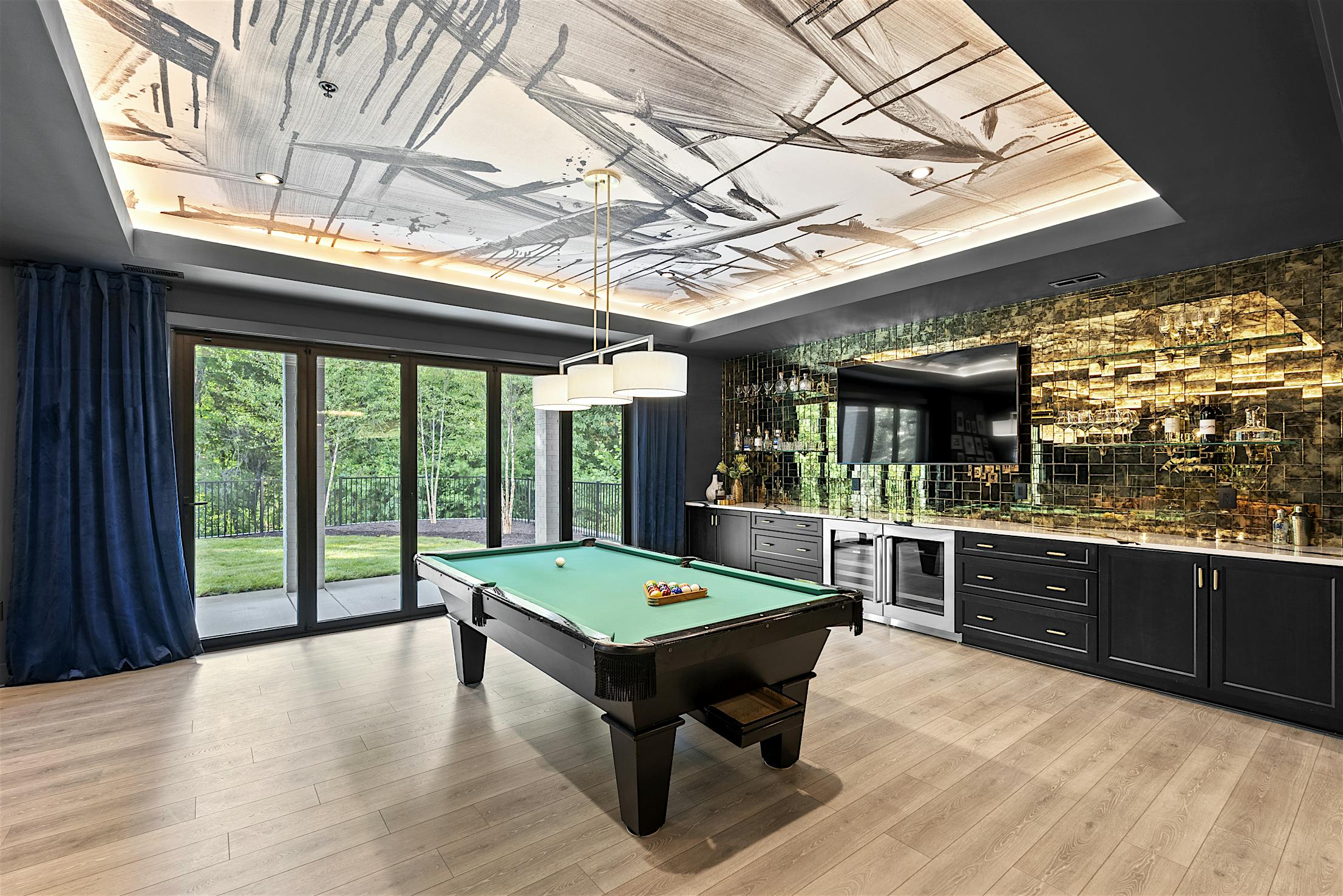 A modern game room with a pool table, black cabinetry, and floor-to-ceiling folding glass doors.