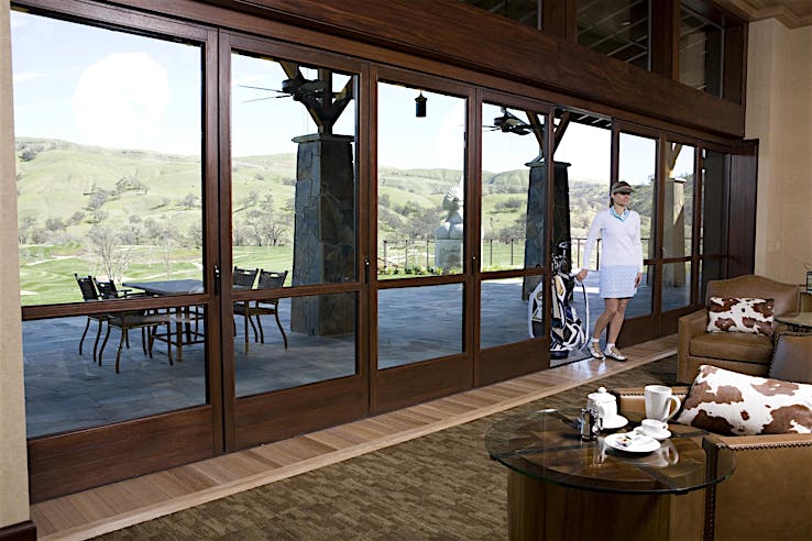 Woman in golf attire approaches a golf club lounge featuring wood-framed sliding glass doors with smooth open-and-close operation.