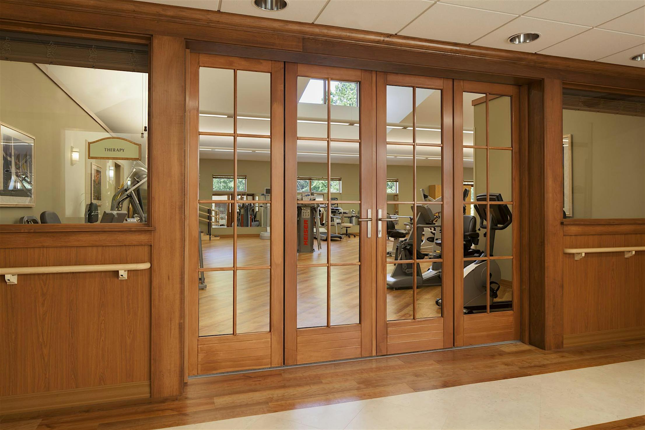 Wood-framed sliding glass doors leading to a modern, well-lit fitness room with treadmills, stationary bikes, and exercise equipment.