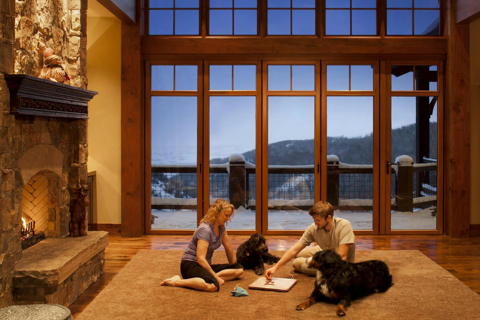 WD65 two people with dogs sitting near the fireplace looking out a wood framed glass wall at the mountains