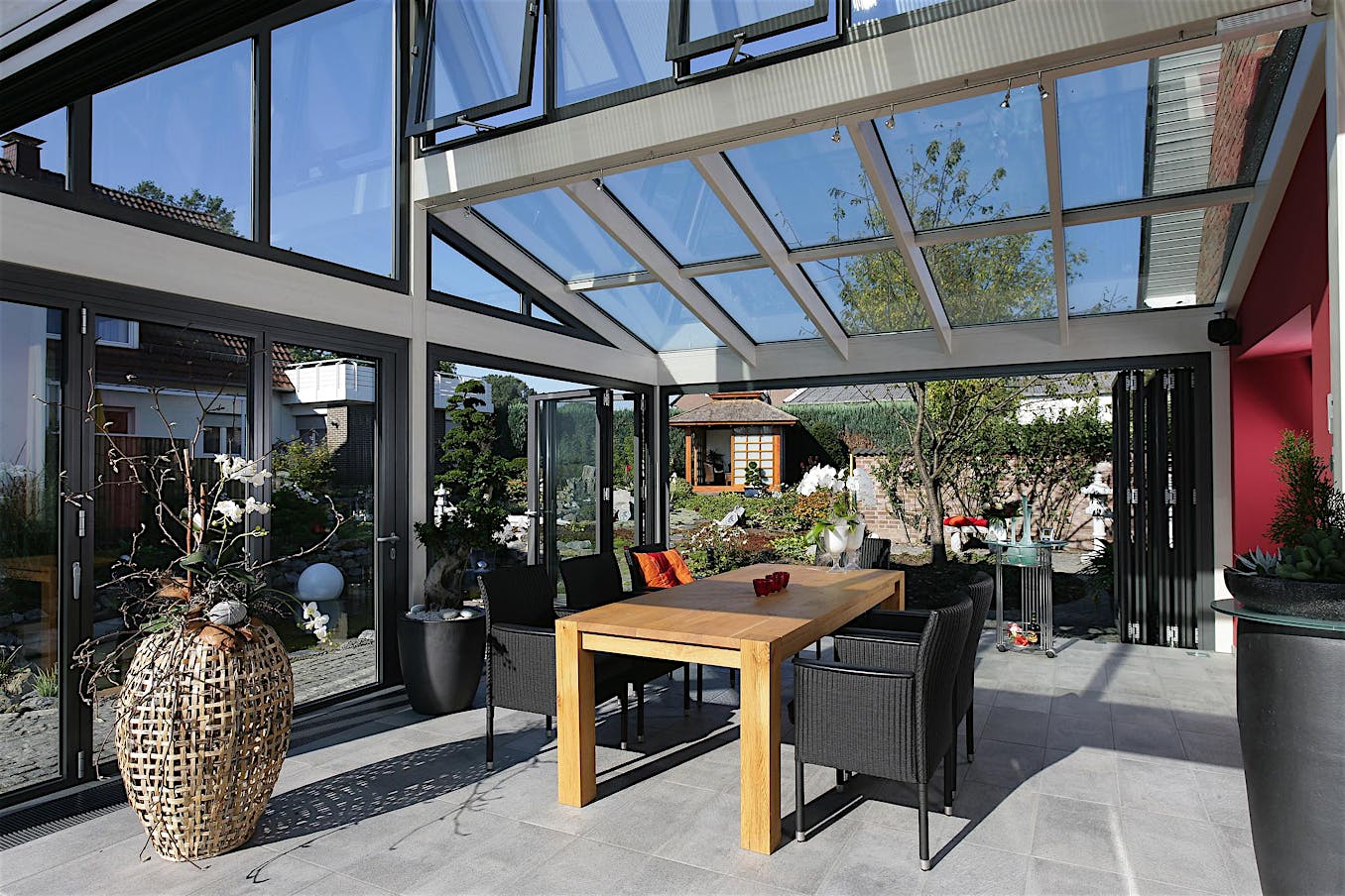 Modern glass-enclosed sunroom featuring folding doors with a wood painted interior and clad exterior opening to a view of the garden outside.