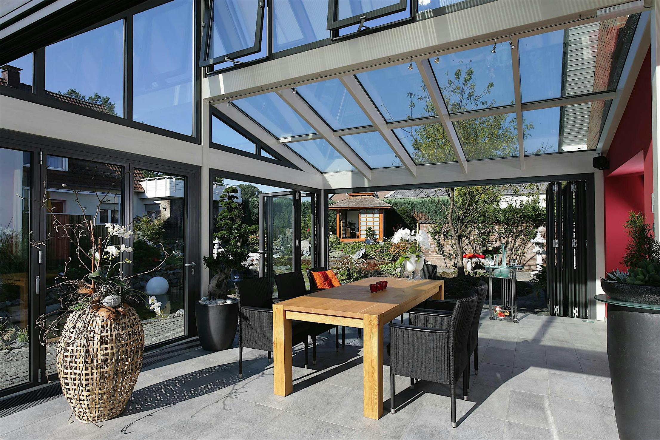 Modern glass-enclosed sunroom featuring folding doors with a wood painted interior and clad exterior opening to a view of the garden outside.