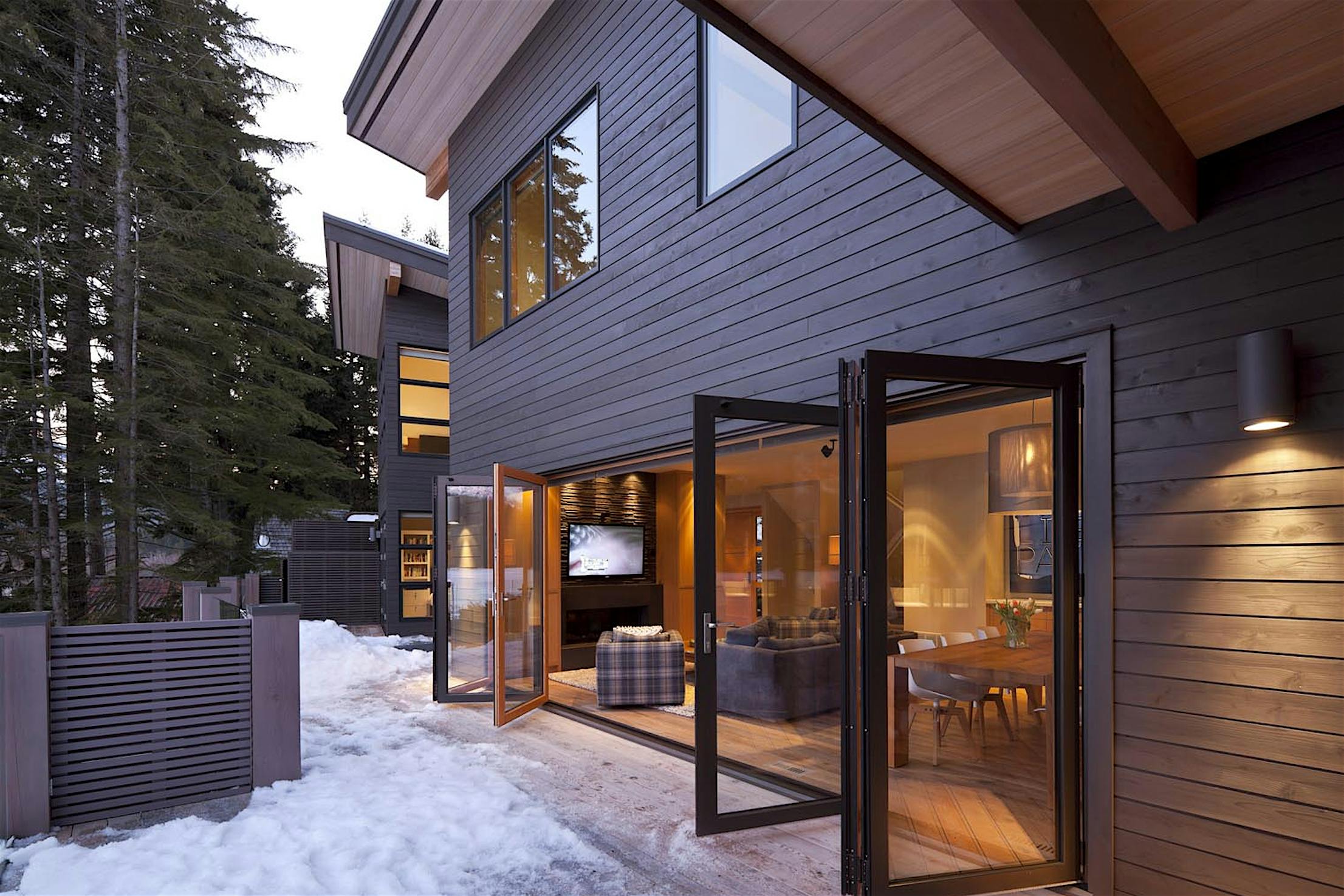 A house in the woods with a wooden deck and aluminum clad folding doors