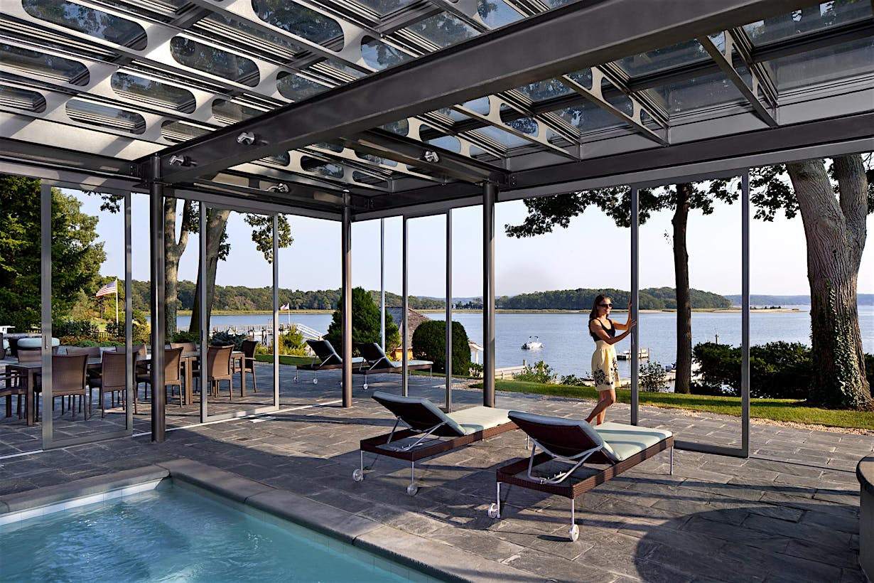 Modern outdoor patio with pool. A women is adjusting the sliding glass door, demonstrating how large openings are possible with unlimited spans of individual panels for an unobstructed view.