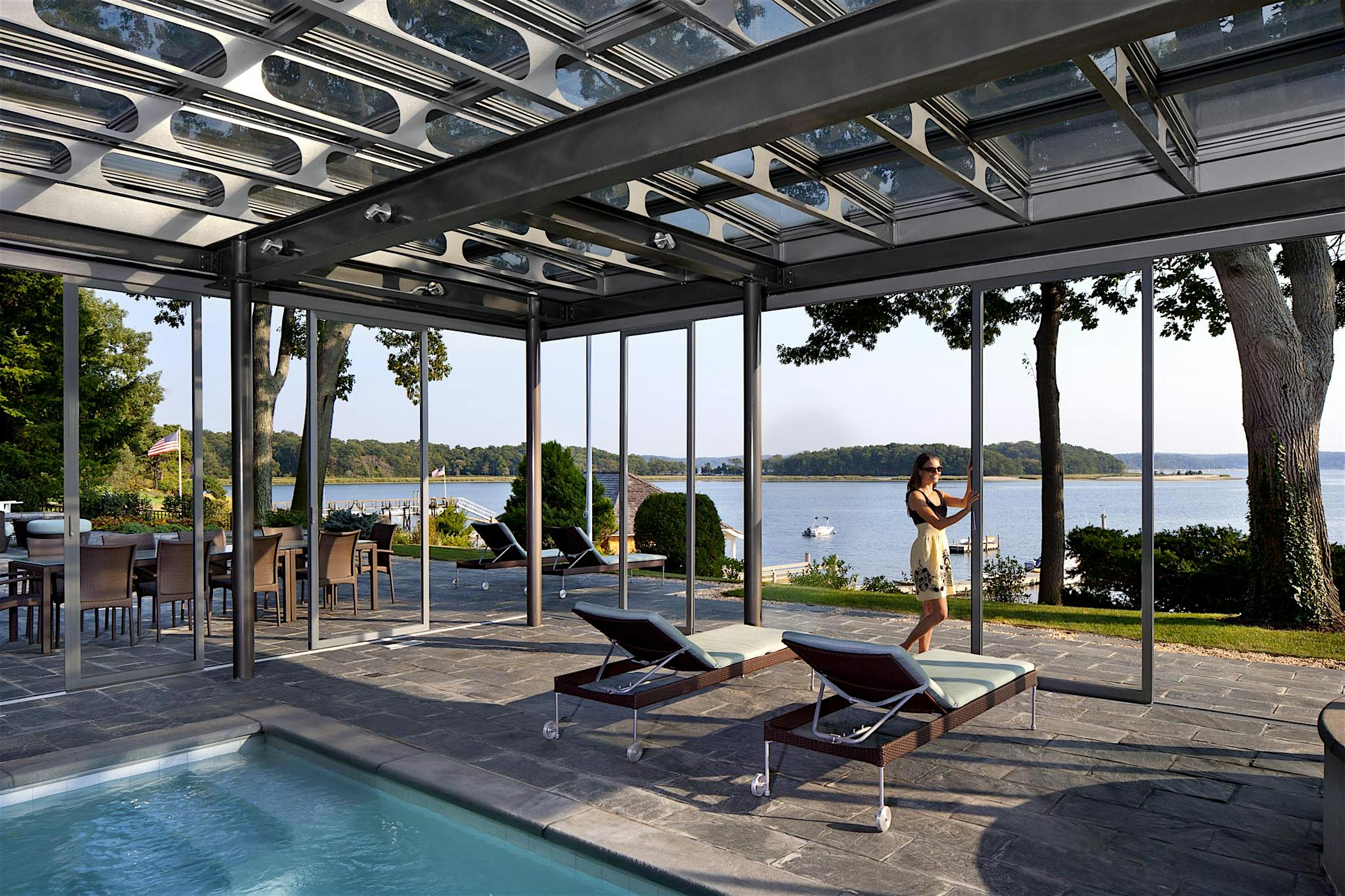 Modern outdoor patio with pool. A women is adjusting the sliding glass door, demonstrating how large openings are possible with unlimited spans of individual panels for an unobstructed view.