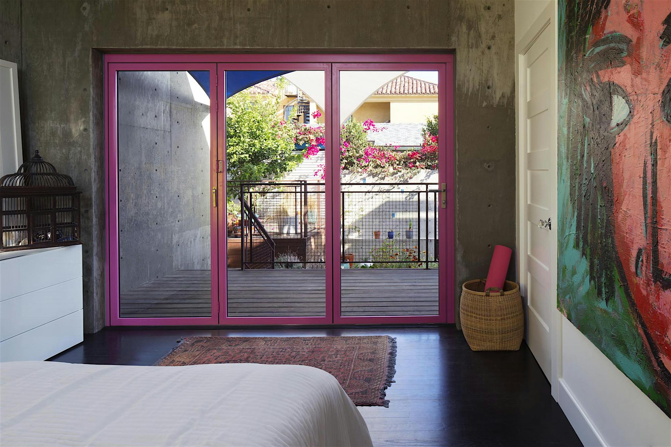 Modern bedroom with dark floors and vibrant pink bifold glass doors opening to a balcony.