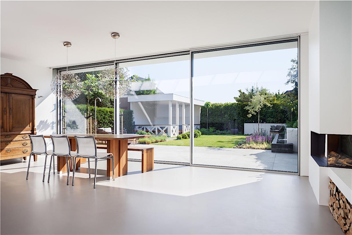Modern dining area with sliding glass doors opening to a green backyard with patio and outdoor seating.