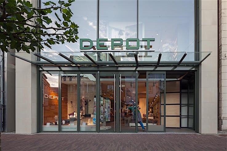 Exterior of DEPOT store with large transom windows and floor-to-ceiling sliding glass doors showcasing modern home décor displays.