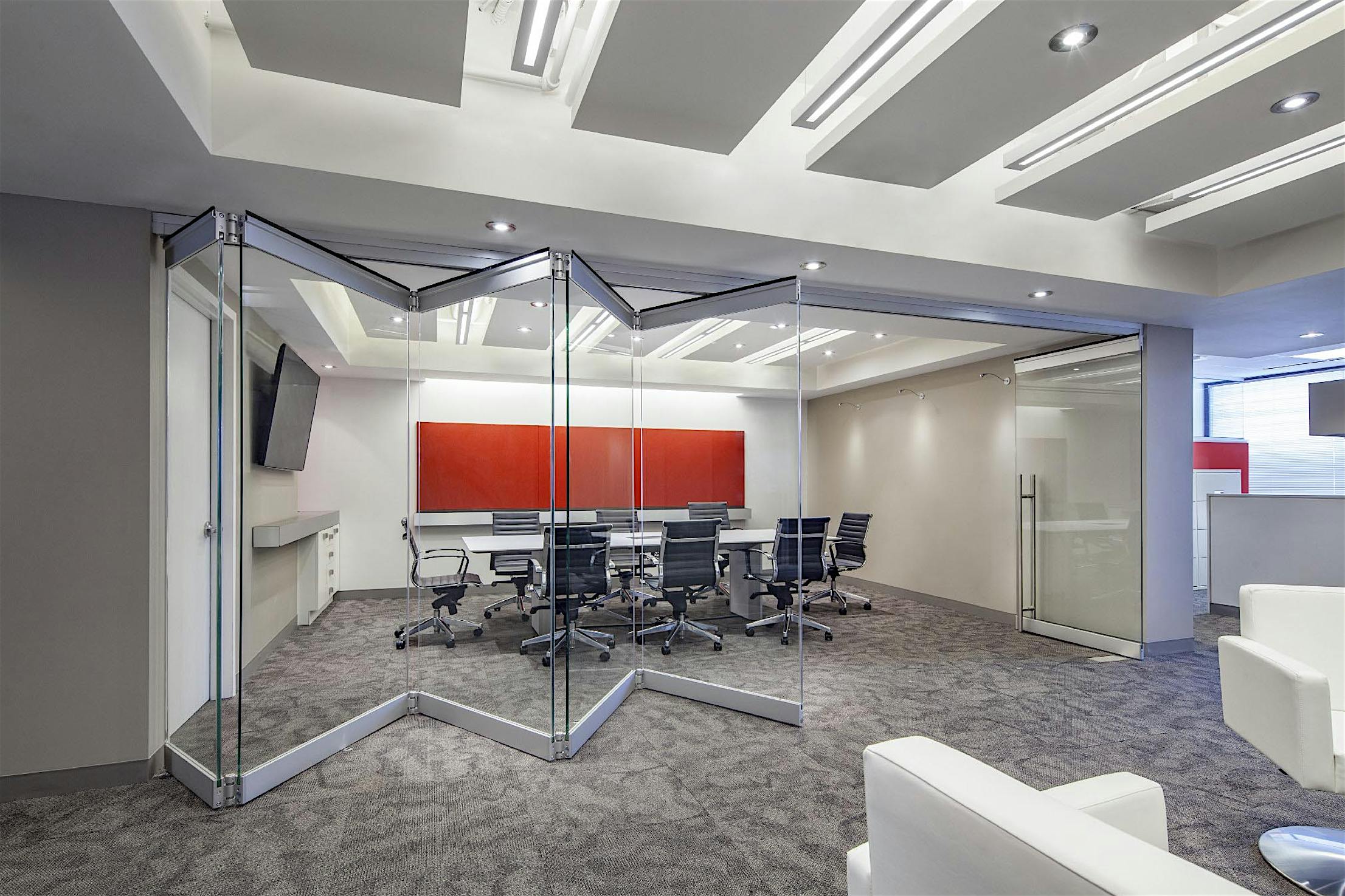 Modern office with frameless folding glass door partitions dividing the workspace from the conference room.
