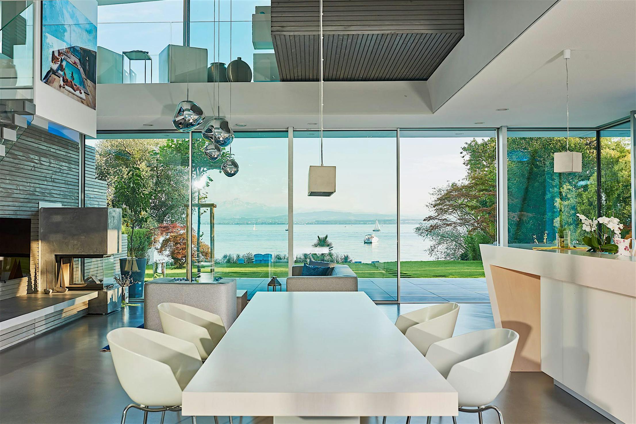 Modern open-plan living and dining area with sliding glass doors opening to scenic lake views with boats and lush trees.