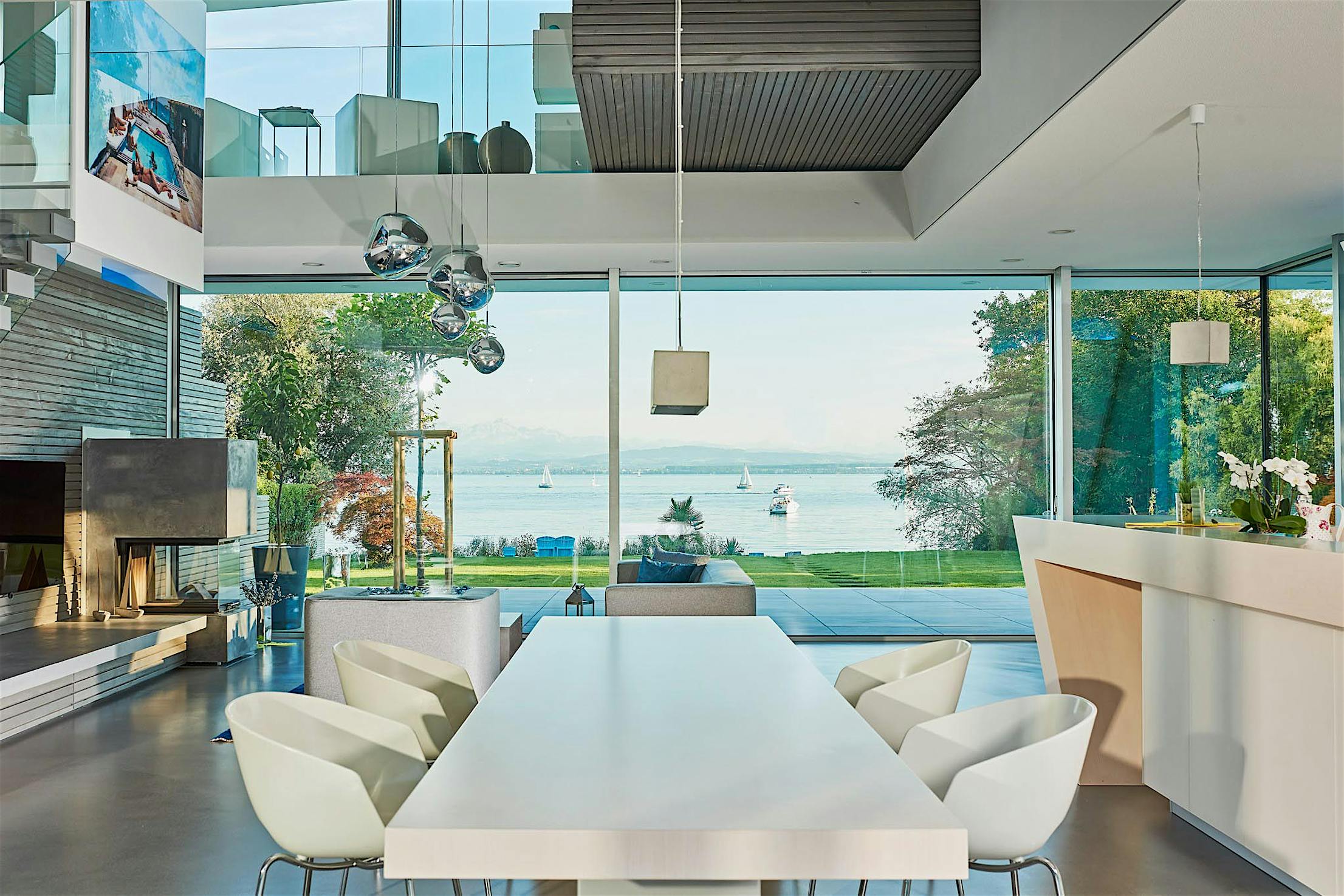 Modern open-plan living and dining area with sliding glass doors, lake views with sailboats, and contemporary decor.