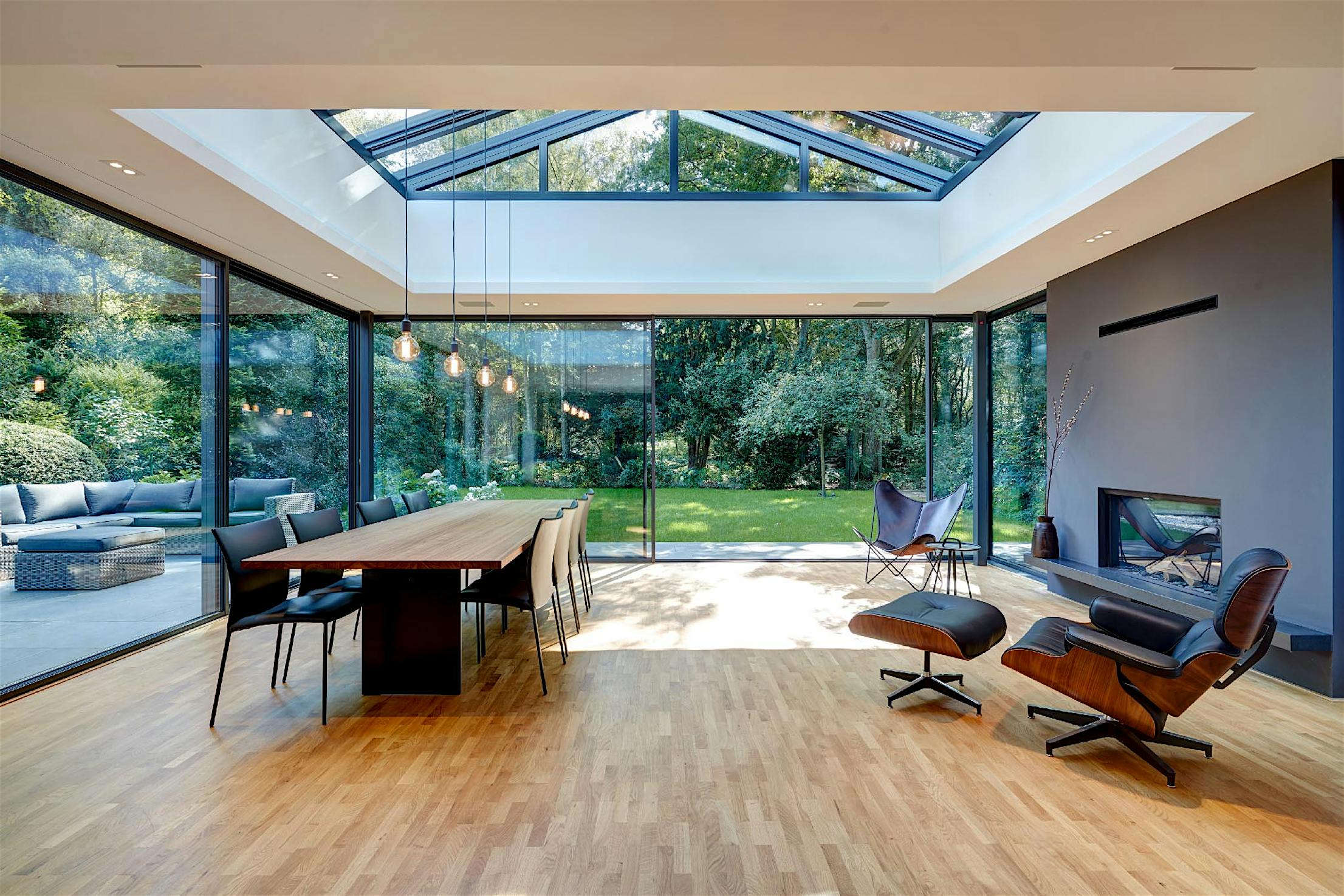 Modern open-plan living and dining area with sliding glass doors, skylight, wooden floors, garden views, and a fireplace.