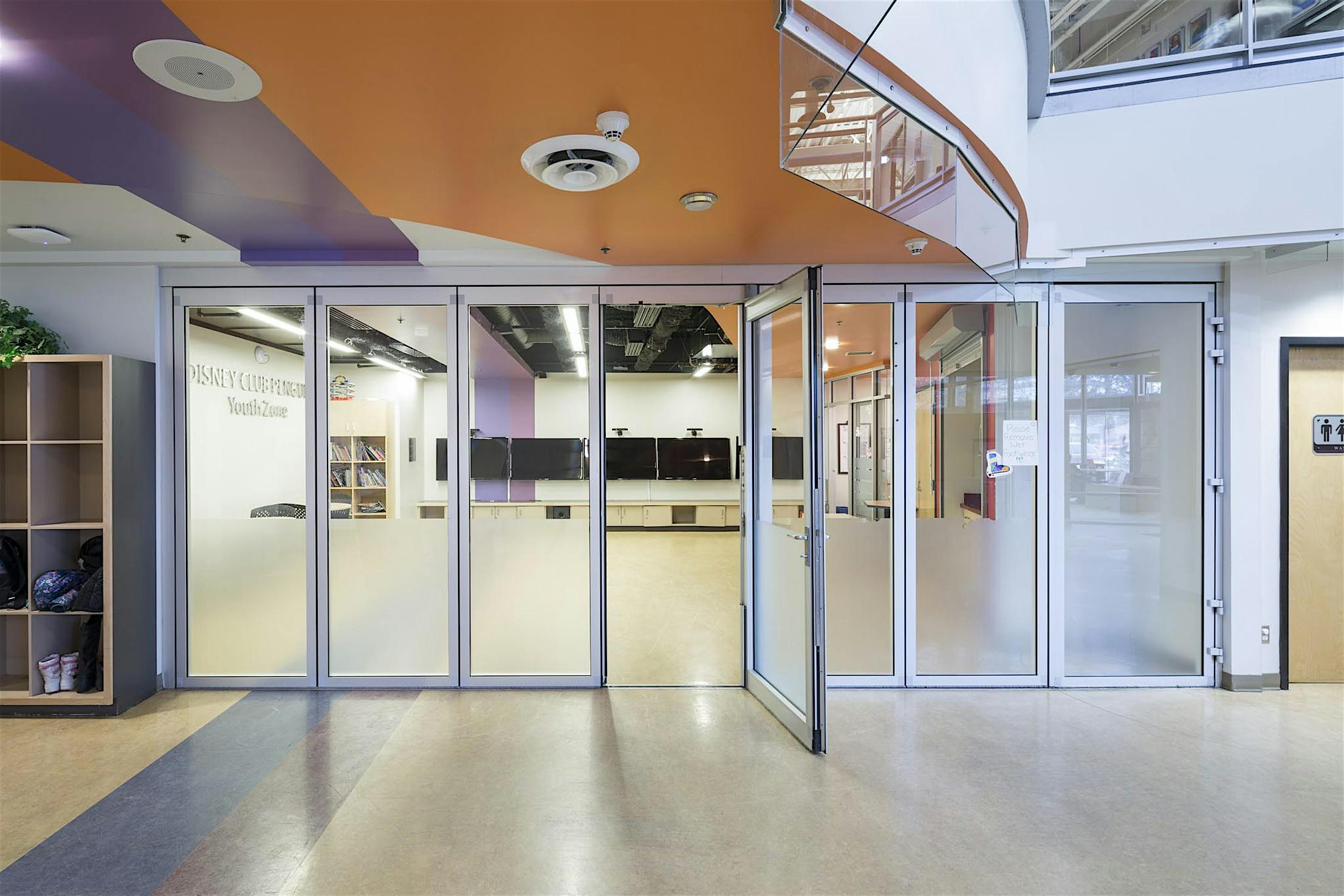 Kelowna YMCA youth zone featuring sliding glass doors, a swing door, frosted lower panels, and an open glass entryway.
