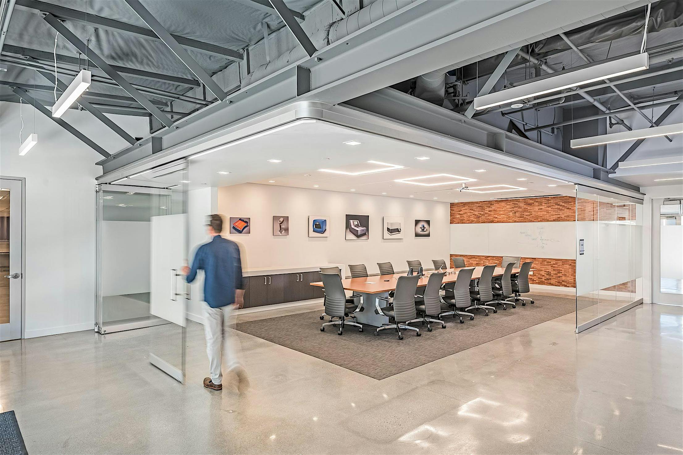 Person smoothly opens sliding glass doors that stack to the side, merging a glass-walled conference room with adjacent space to create a larger, flexible meeting area.