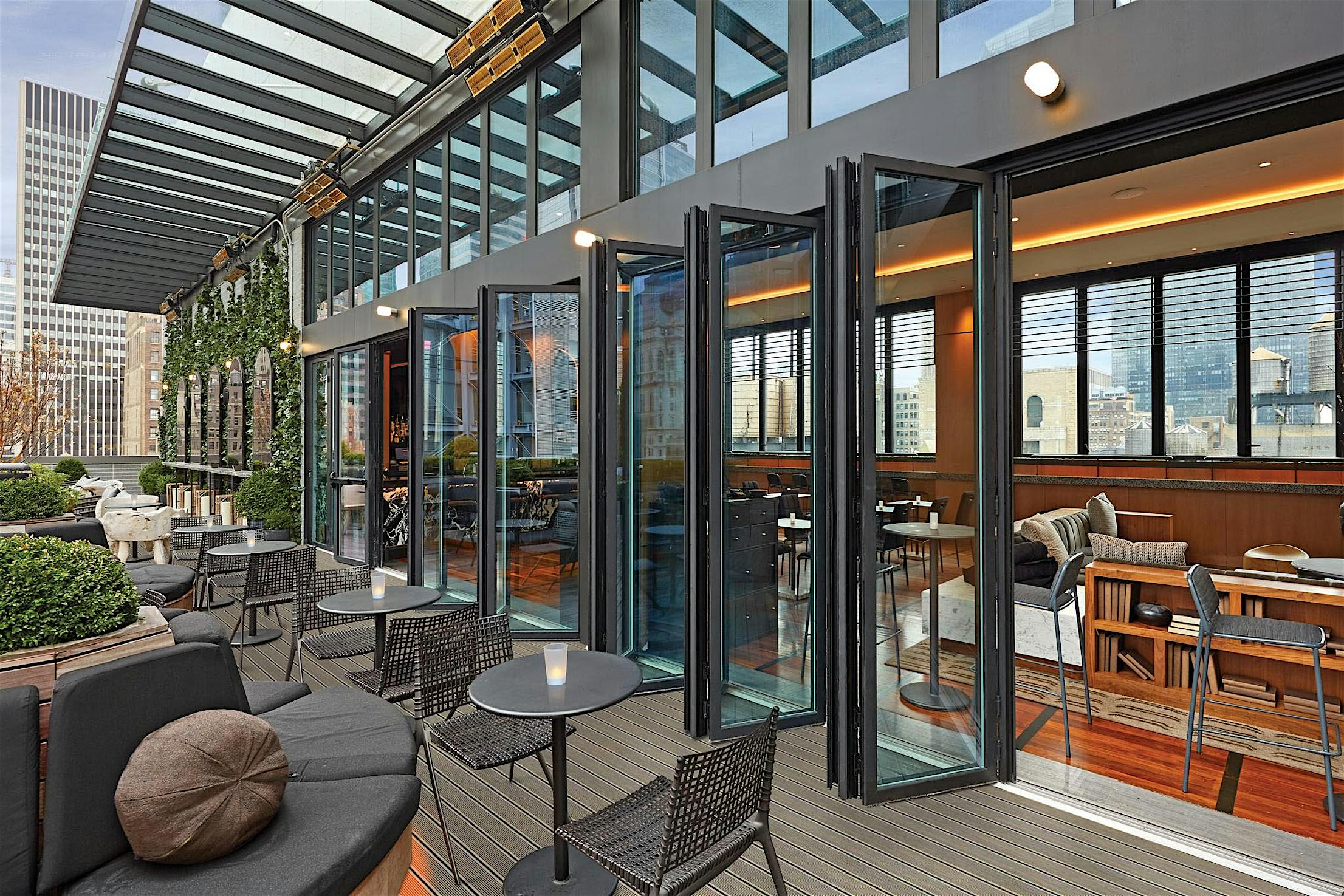 Rooftop restaurant with indoor-outdoor space. Indoor area visible through open folding glass doors, boasts wooden furniture and décor for a cozy atmosphere.