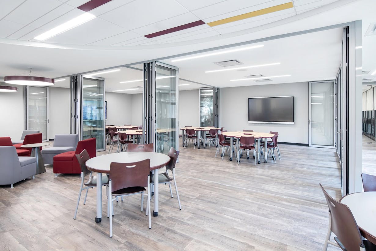 A classroom with tables and chairs equipped with acoustical folding glass panels