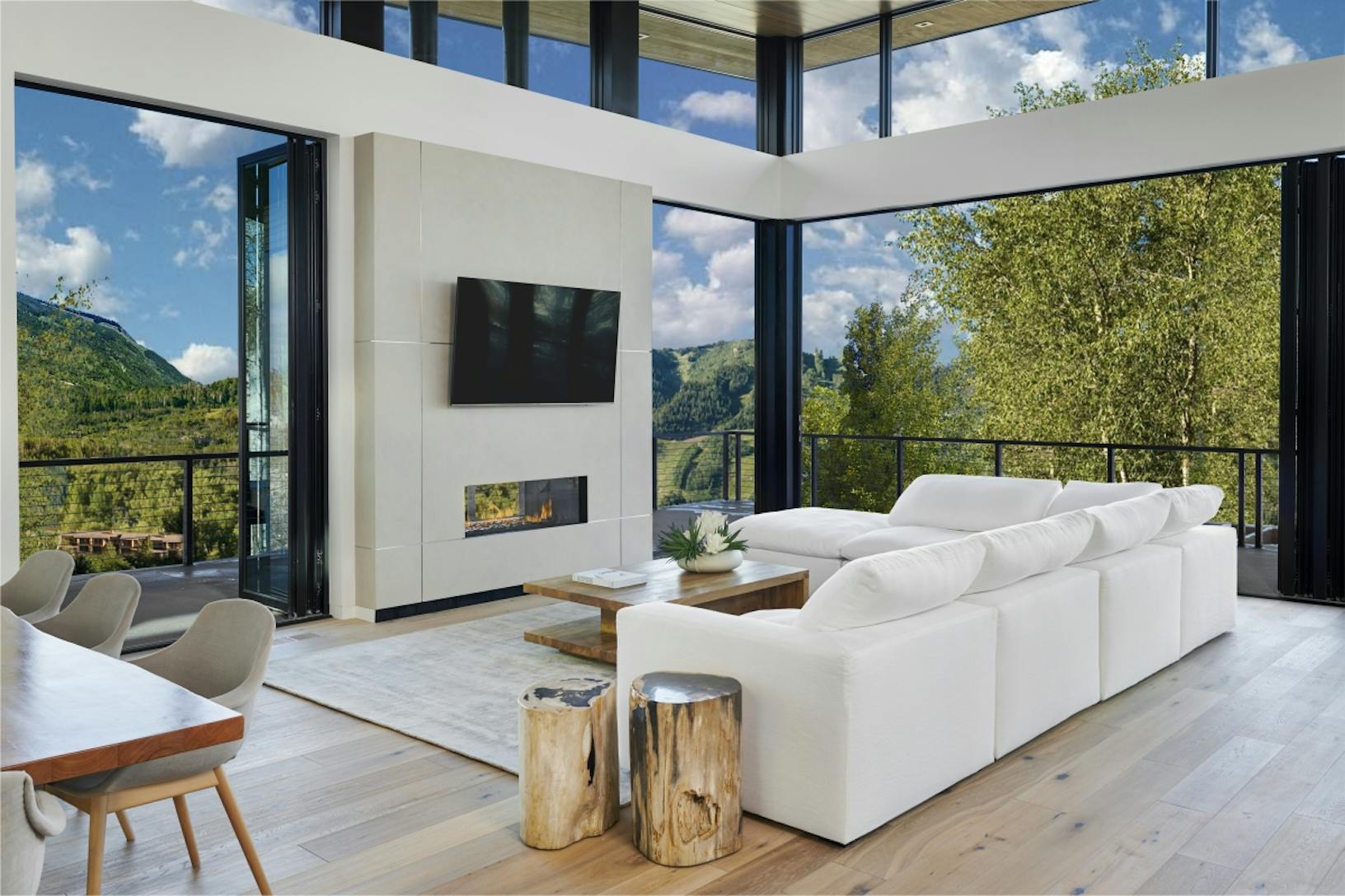 Modern living room with folding patio doors and large windows offering a panoramic view of a forested mountain landscape