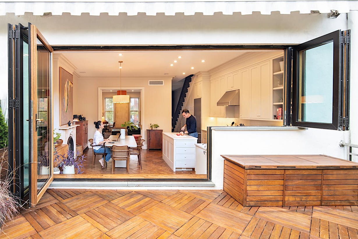 Modern kitchen and dining area with wood-clad folding glass doors that open to a stylish outdoor patio for seamless indoor-outdoor living.