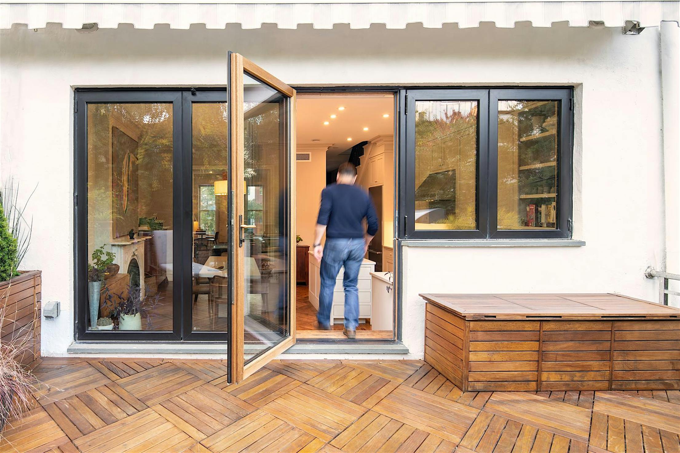 Person entering a modern home through open wood-framed swing doors from a wooden deck patio.